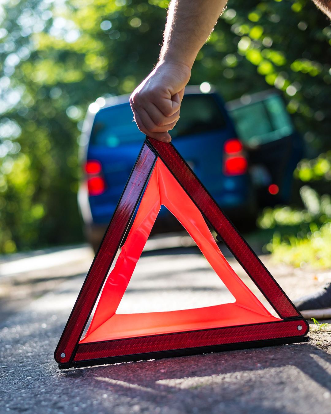 Eine Hand stellt ein Warndreieck auf der Straße auf